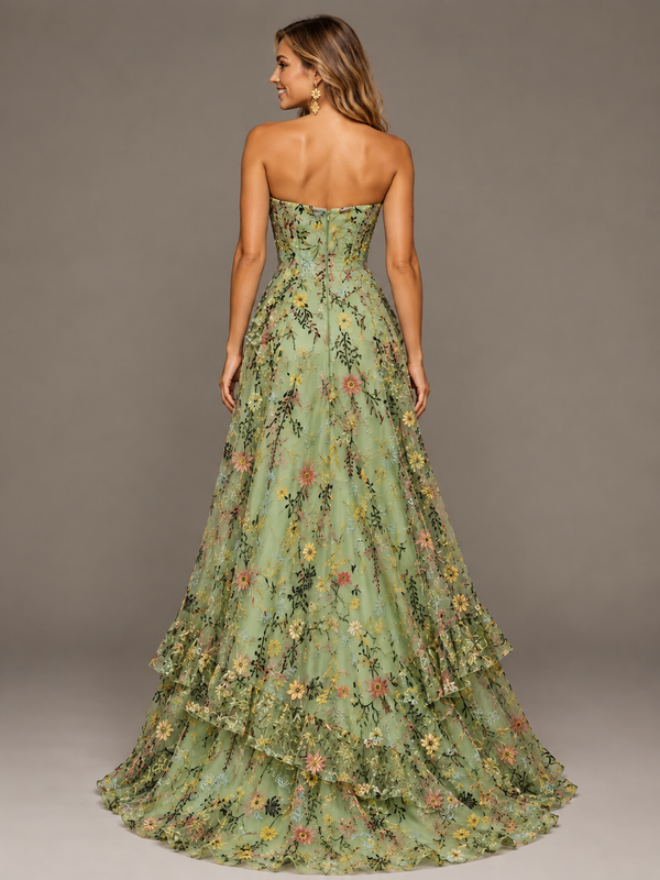 Back view of a woman wearing a sage green floral embroidered strapless evening gown with layered full skirt and train